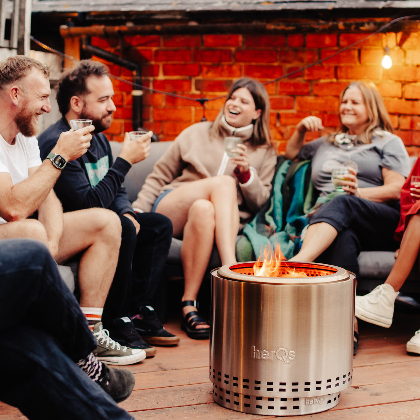 Gezelschap met een drankje rond een brandende herQs vuurkorf